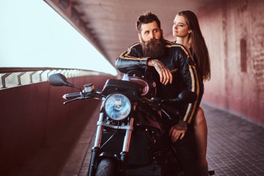 Vahşi motorcu siyah deri ceket ve özel yapım bir retro motosiklet üzerinde bir köprü altında bir footway birlikte oturan seksi esmer kız sakallı.