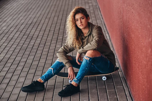 若い女性の肖像画のパーカーを着たし 橋通行でスケート ボードの上に座ってジーンズをリッピング — ストック写真