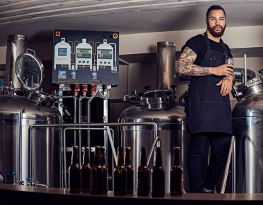 Bir şık sakallı dövmeli koyu tenli erkek portresi bir bardak bira, bira tezgahın arkasındaki ayakta tutan