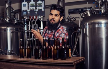 Şık tam Hintli bir yün gömlekli sakallı ve önlük bir bardak bira, bira fabrikası tezgahın arkasındaki ayakta tutan.