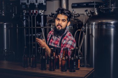 Şık tam Hintli bir yün gömlekli sakallı ve önlük bir bardak bira, bira fabrikası tezgahın arkasındaki ayakta tutan.