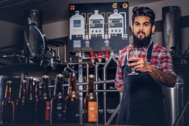 Şık tam Hintli bir yün gömlekli sakallı ve önlük bir bardak bira, bira fabrikası tezgahın arkasındaki ayakta tutan.