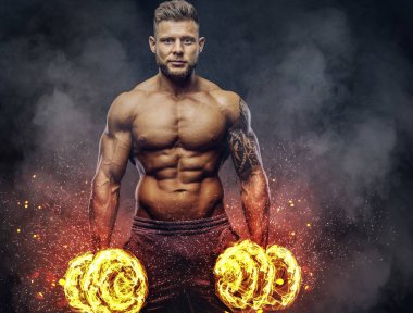 Dumbbells ile egzersizleri yapıyor güçlü şık vücut geliştirmeci, kolundaki dövme ile. Yangın sanat kavramı.