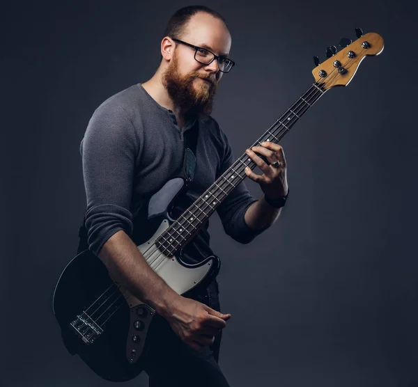 Redhead bearded male musician wearing glasses dressed in a gray t-shirt playing on electric guitar. Isolated on a gray background.