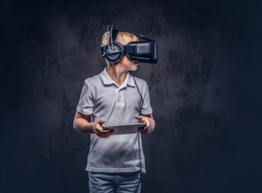 Liseli Sarışın sanal gerçeklik gözlük takan ve dijital tablet kullanma beyaz bir t-shirt giymiş. Karanlık dokulu bir arka plan üzerinde izole.