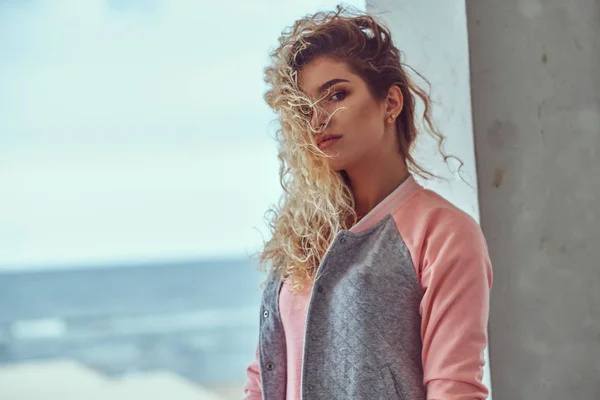 ピンクの シャツとジャケットの海岸に対するポーズに身を包んだ金髪巻き毛を持つ官能的な若い女の子のクローズ アップの肖像画 — ストック写真