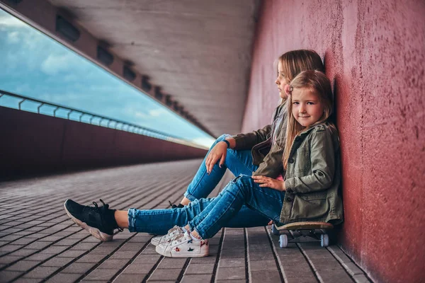 橋通行でスケート ボードに座って壁にもたれトレンディな服を着て つの小さな姉妹の肖像 — ストック写真