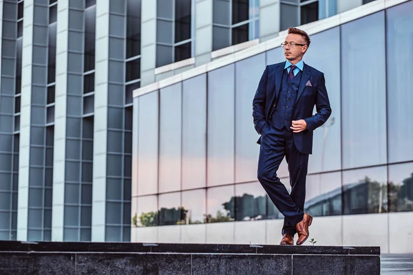 一个充满自信的男人在一个优雅的西装摆在口袋里的肖像与摩天大楼背景的完整身体画像. — 图库照片