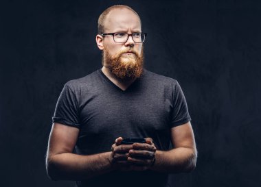 Kızıl saçlı portresi yakından ile ısınma bir fincan kahve koyu dokulu bir arka plan üzerinde izole bir gri t-shirt giymiş Gözlüklü erkek ayakta sakallı.