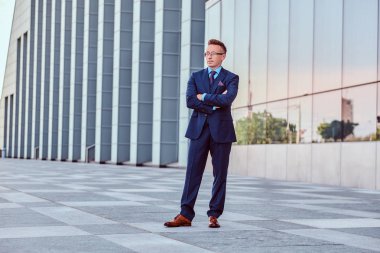 Şık takım elbise ayakta cityscape arka plan karşı çapraz kolları olan kendine güvenen işadamı giymiş.