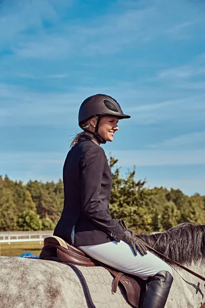 Retrato de una jinete sonriente sobre un caballo gris manzana en la arena abierta . —  Fotos de Stock