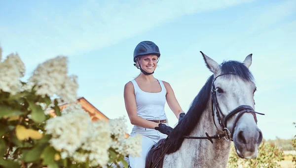 Jockey femenino sonriente sobre caballo gris manzana caminando por el jardín floreciente . —  Fotos de Stock