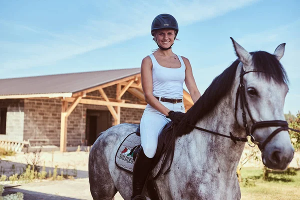 Smiling female jockey on dapple gray horse walking through the flowering garden. — Stock Photo, Image