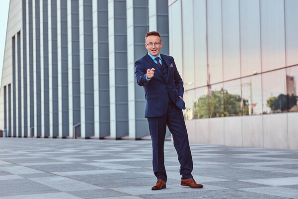 Happy confident businessman dressed in an elegant suit standing outdoors against cityscape background.