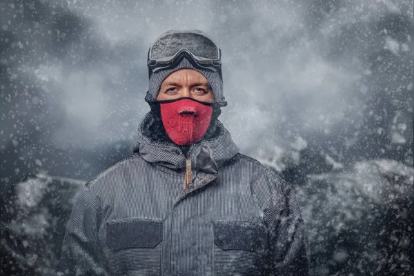 Portrait of a snowboarder dressed in a full protective gear for extream snowboarding against the background of mountains.
