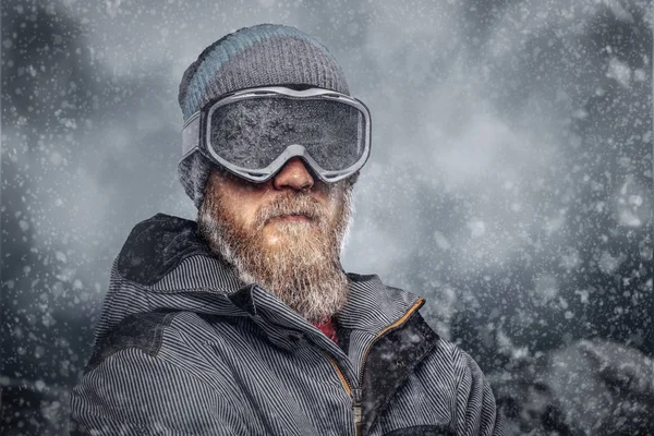 一个红发滑雪板的肖像 在冬天的帽子和保护眼镜穿着滑雪板大衣摆在山的背景上的一个完整的胡子 — 图库照片