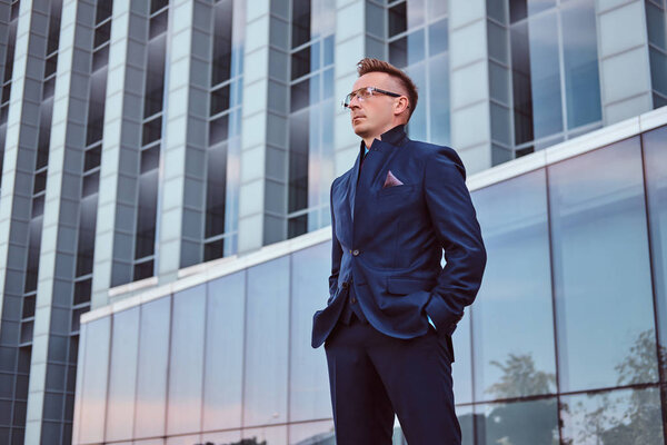 Modern businessman. Low angle view of confident handsome man in an elegant suit looking away while standing outdoors against skyscraper background.