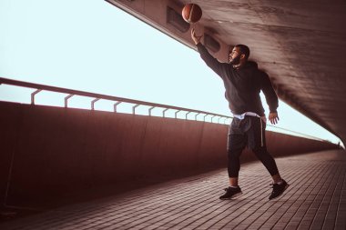 Esmer adam portresi köprü altında bir footway basketbol oynamak siyah bir hoodie ve spor şort giymiş.