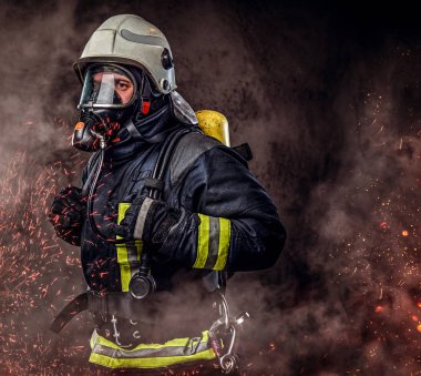Portre üniforma ve yangın bir oksijen maskesi ayakta giymiş itfaiye eri ve kıvılcım ve karanlık bir arka plan üzerinde duman.