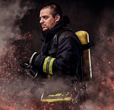 Bir itfaiyeci onun geri yangında duran üzerinde bir oksijen tankı ile kıvılcım ve karanlık bir arka plan üzerinde duman.