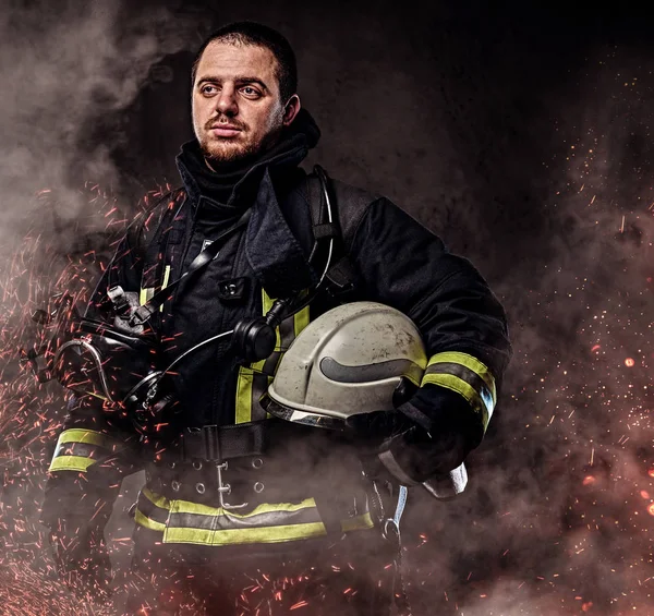 一个穿着制服的职业消防员 在黑暗的背景下 在火灾中的火花和烟雾中戴着安全帽 — 图库照片