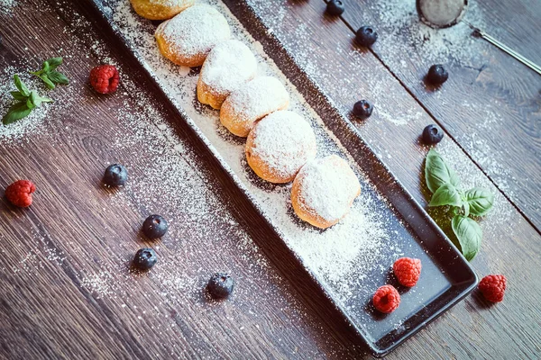 Yakın çekim fotoğraf kümesi Donuts ahududu bilberry ve nane ile siyah uzun tabakta pudra şekeri serpilir.