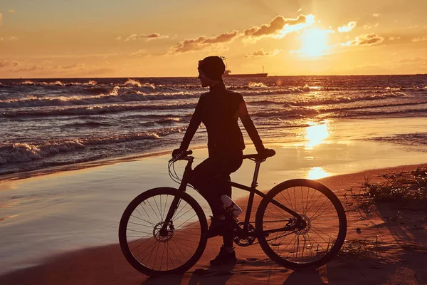 Female cyclist standing with her bicycle and enjoying the sunset on the sea coast. — Stock Photo, Image