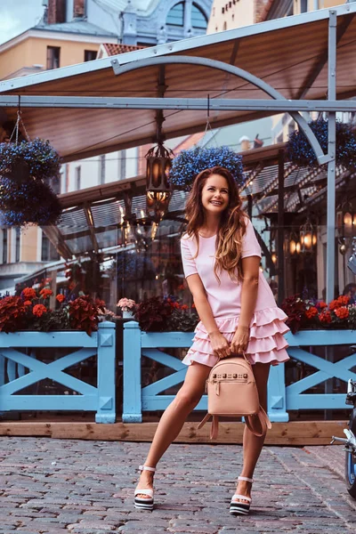 幸せな中年の女性を着たピンクのドレスと靴の高い裏にリュックサック アウトドア カフェの近くでポーズ — ストック写真