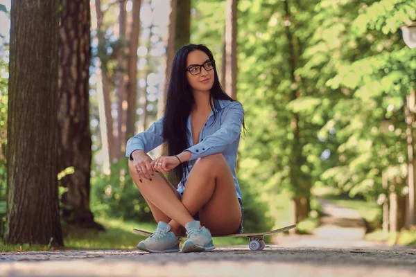 シャツと公園でスケート ボードの上に座ってパンツを身に着けているガラスの豪華な官能的なブルネットの少女 — ストック写真