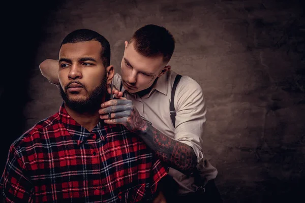 老式的专业纹身理发师用剪刀和梳子给非洲裔美国人的客户理发 在深色纹理背景下隔离 — 图库照片