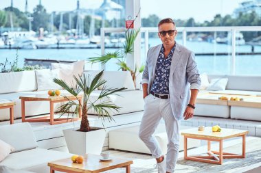 Şehir wharf arka planı açık restoranda modern zarif elbise giymiş şık saç ile moda zengin adam.