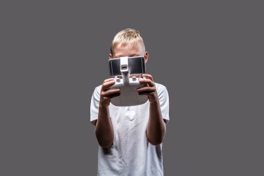 Sarı saçlı beyaz bir t-shirt giymiş yakışıklı küçük çocuk boksör quadcopter kontrol uzak tutar. Gri bir arka plan üzerinde izole.