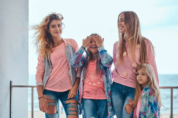 Retrato de una familia alegre vestida con ropa de moda posando cerca de una barandilla contra la costa del mar . —  Fotos de Stock