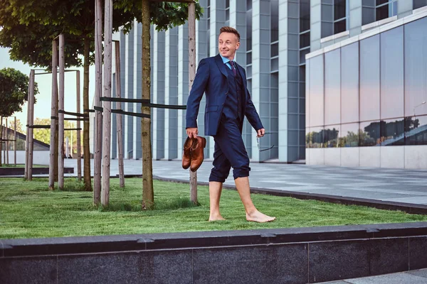 우아한 옷 입고 자신감 사업 도시 배경 녹색 잔디밭에 맨발로 서 있는 동안 그의 신발을 보유합니다. — 스톡 사진