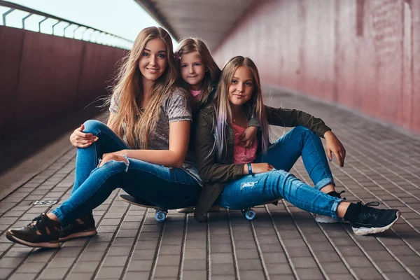 Porträt einer attraktiven Familie. Mutter und ihre Töchter sitzen zusammen auf einem Skateboard am Brückensteg. — Stockfoto