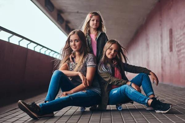 Porträt einer attraktiven Familie. Mutter und ihre Töchter sitzen zusammen auf einem Skateboard am Brückensteg. — Stockfoto