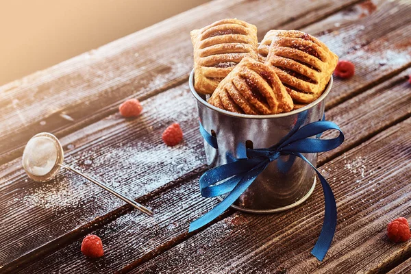 Close-up foto van een bladerdeeg met jam in een emmer versierd met een blauw lint op houten planken met frambozen en bestek. — Stockfoto