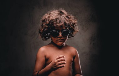 Sevimli küçük gömleksiz çocuk yüzme bir stüdyoda poz gözlükler. Karanlık dokulu bir arka plan üzerinde izole.