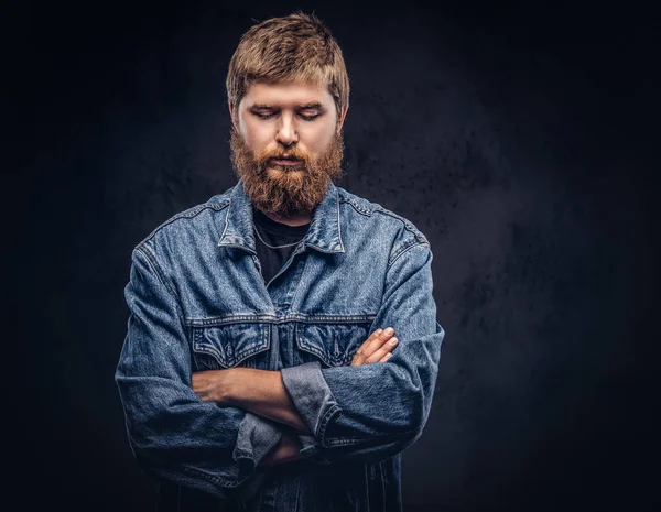Porträtt av en stilig hipster kille klädd i Jeansjacka poserar med korsade armar på en mörk bakgrund. — Stockfoto
