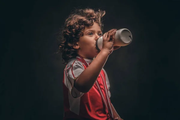 小冠军男孩在运动衫与金牌喝水从瓶子 在深色纹理背景下隔离 — 图库照片