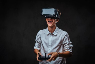 Neşeli genç bir beyaz gömlek giymiş sanal gerçeklik gözlükleri ve denetimleri uzaktan denetimi kullanarak quadcopter giyer. Koyu arka plan üzerinde izole.
