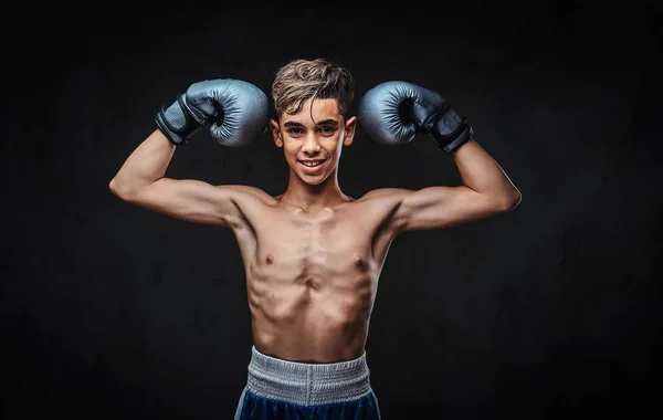Jovem boxeador sem camisa sorridente usando luvas mostrando músculos. Isolado em um fundo escuro . — Fotografia de Stock