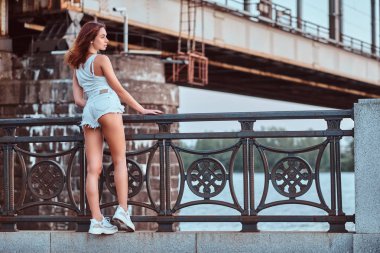 Şort ve tişört üzerinde bir köprü karşı dolgu, Otokorkuluk yaslanmış bir şehvetli kız arkadan görünüm giymiş.