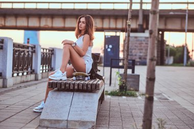 Şort ve tişört üzerinde dolgu güzel gün batımı sırasında oturan genç şehvetli patenci kız giymiş.