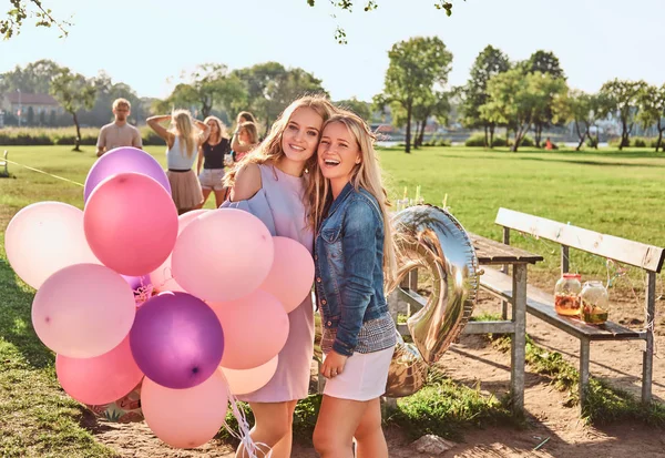 Novia sonriente posando con globos cerca de una mesa celebrando un cumpleaños en el parque al aire libre . —  Fotos de Stock