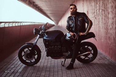 Bununla birlikte güneş gözlüklü bir siyah deri ceket giymiş şık şık motorcu bir kameraya bakarak onun ısmarlama retro motosiklet üzerinde oturan bir kask tutar.