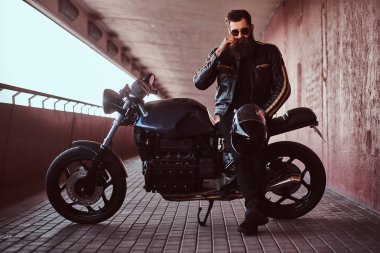 Bununla birlikte güneş gözlüklü bir siyah deri ceket giymiş şık şık motorcu bıyık düzeltmek ve kask ısmarlama retro motosikletine otururken bir kameraya bakıyor tutar.