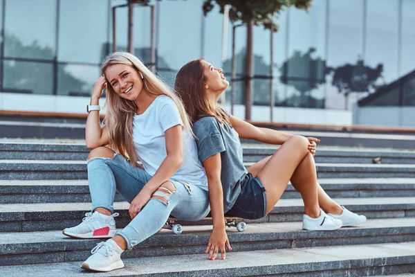 Két Fiatal Hipster Lányok Együtt Ültek Egy Gördeszka Háttérben Felhőkarcoló — Stock Fotó