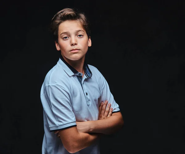 Portrait of a teenager dressed in a white t-shirt standing with crossed arms. Isolated on a dark background.