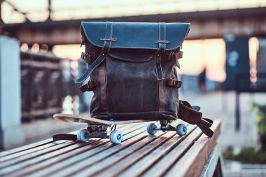 Bir kaykay üzerinde yalan bir sırt çantası, yakın çekim fotoğraf bu dolgu bir bankta güzel bir gün batımı sırasında duruyor.